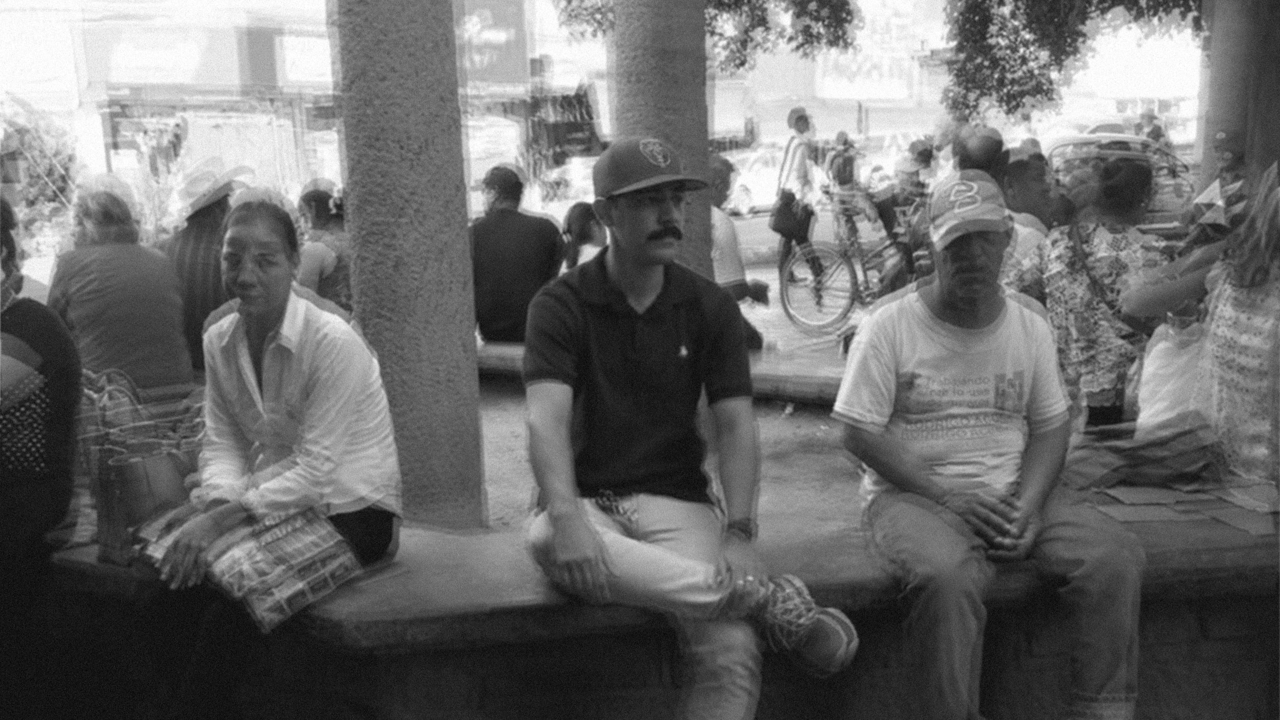 A candid black and white photograph of Reneshizzle sitting in a public square with locals, capturing a moment of everyday life and personal connection.