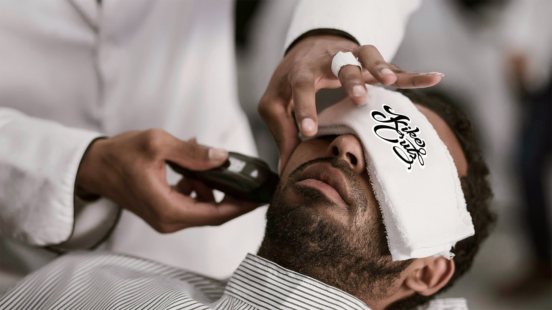 A close-up of a barber performing a precision straight-razor shave on a client using a Kike Cutz branded neck strip.