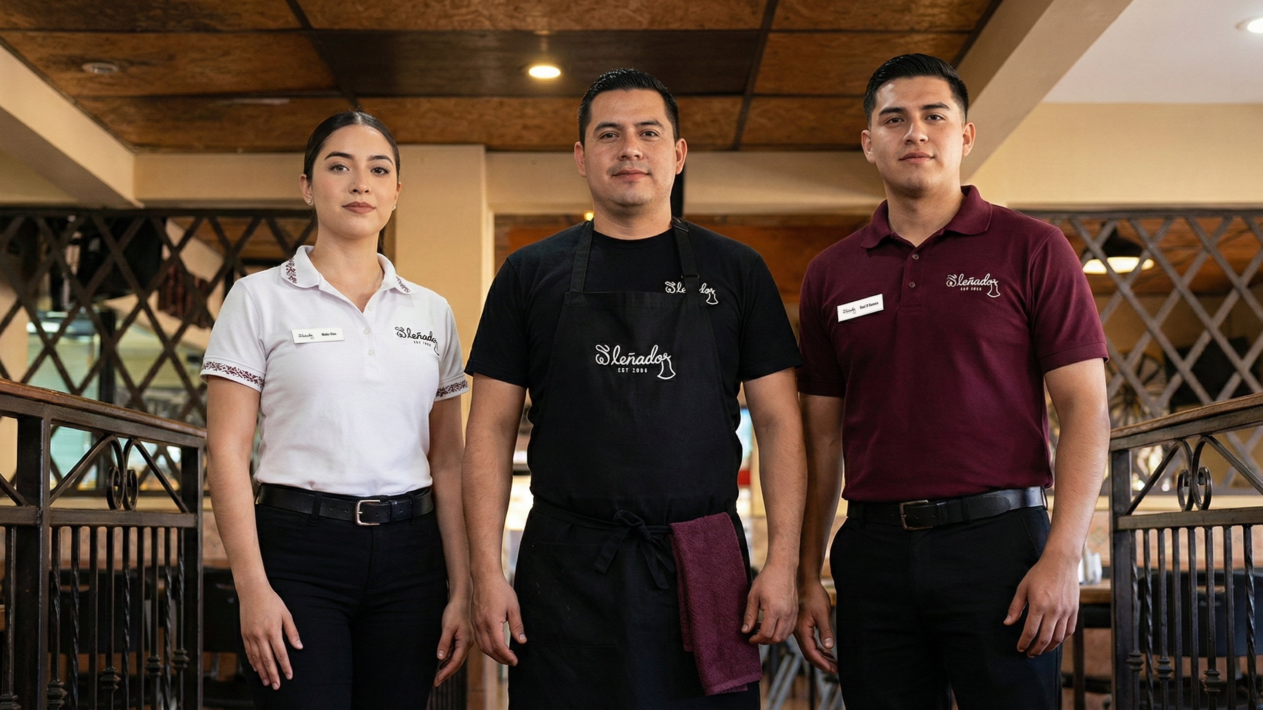 Three employees standing in a restaurant or bar wearing the branded El Leñador uniform with branded embroidery and nametags.