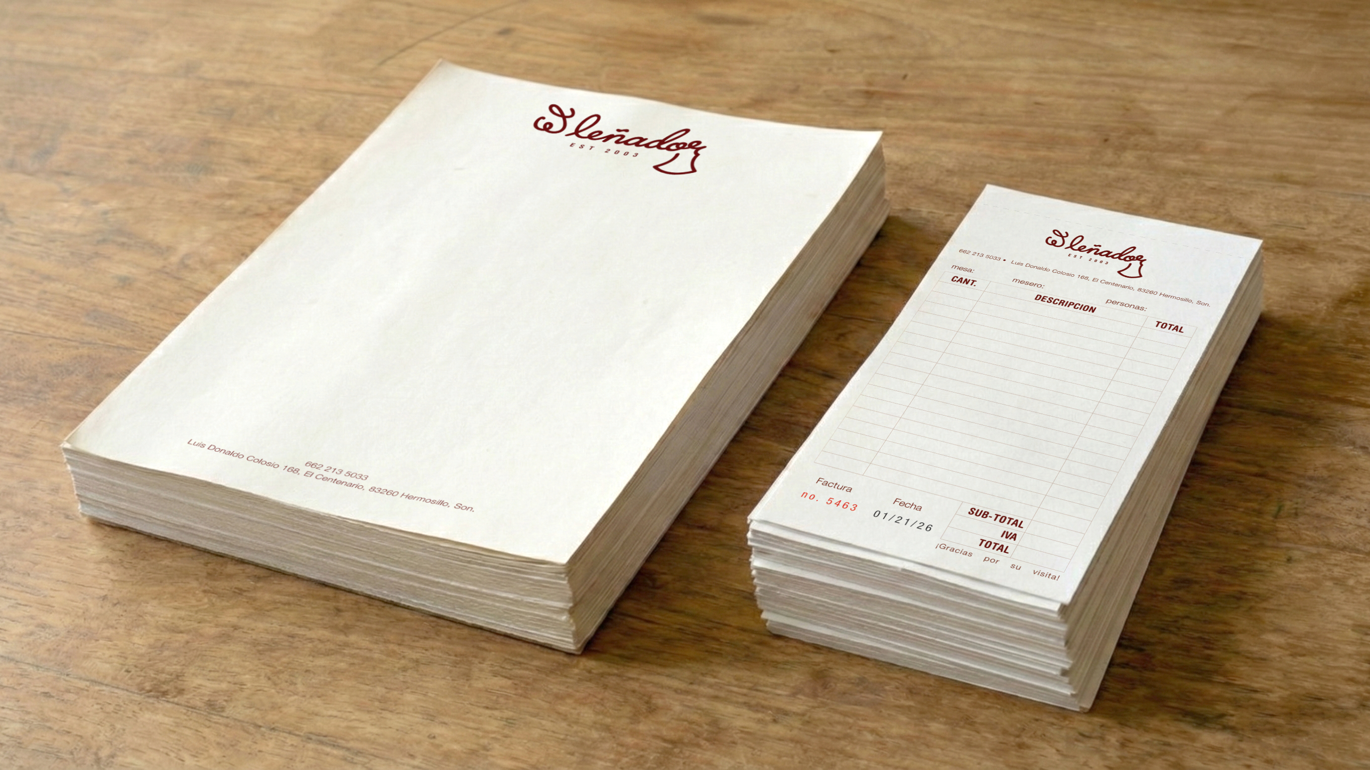 Branded notepads and invoice blocks with the 'El Leñador' logo placed on a wooden table.