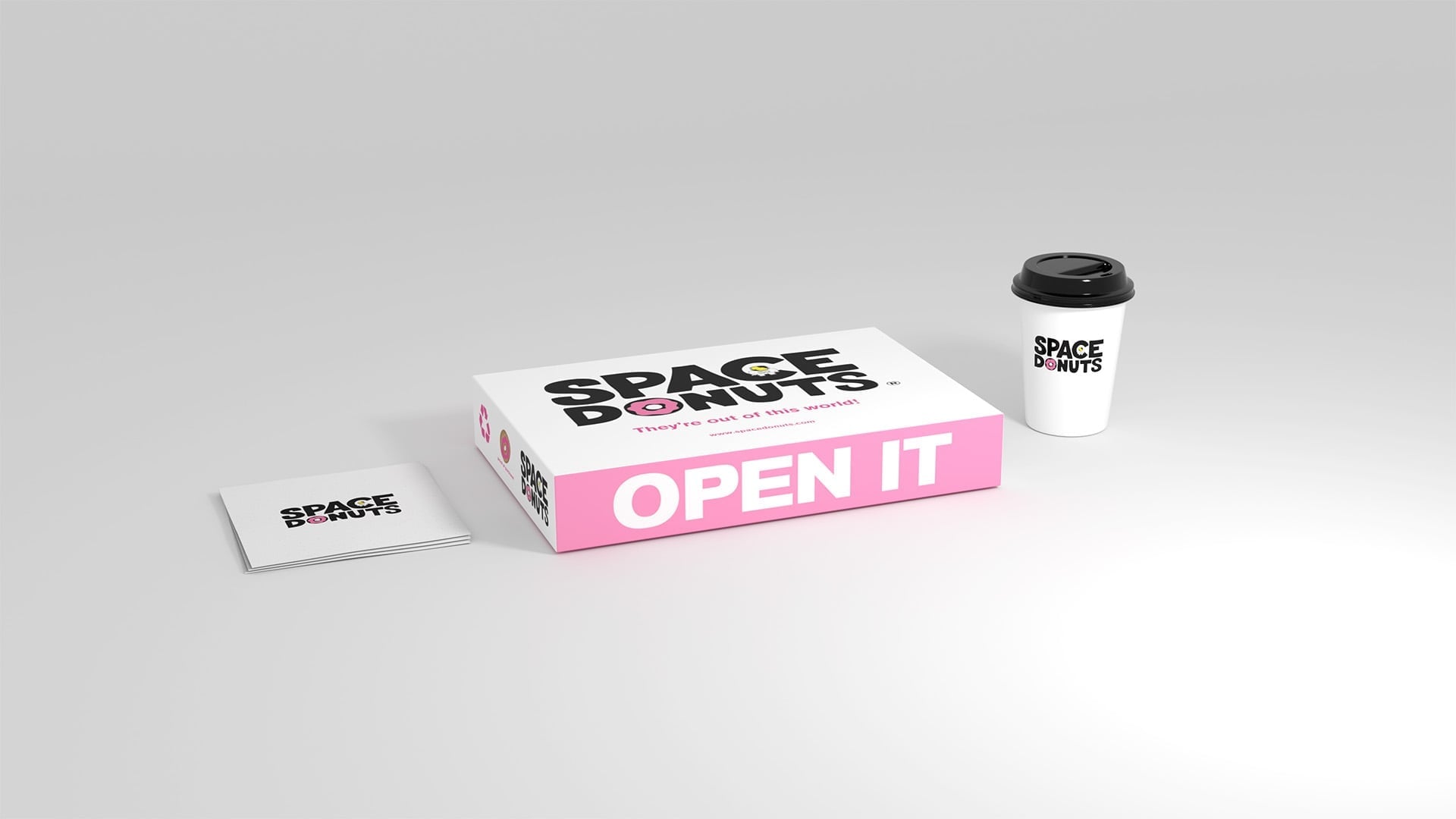 Premium packaging mockup for Space Donuts, including a pink-sided donut box, branded coffee cup, and business card on a clean studio background.